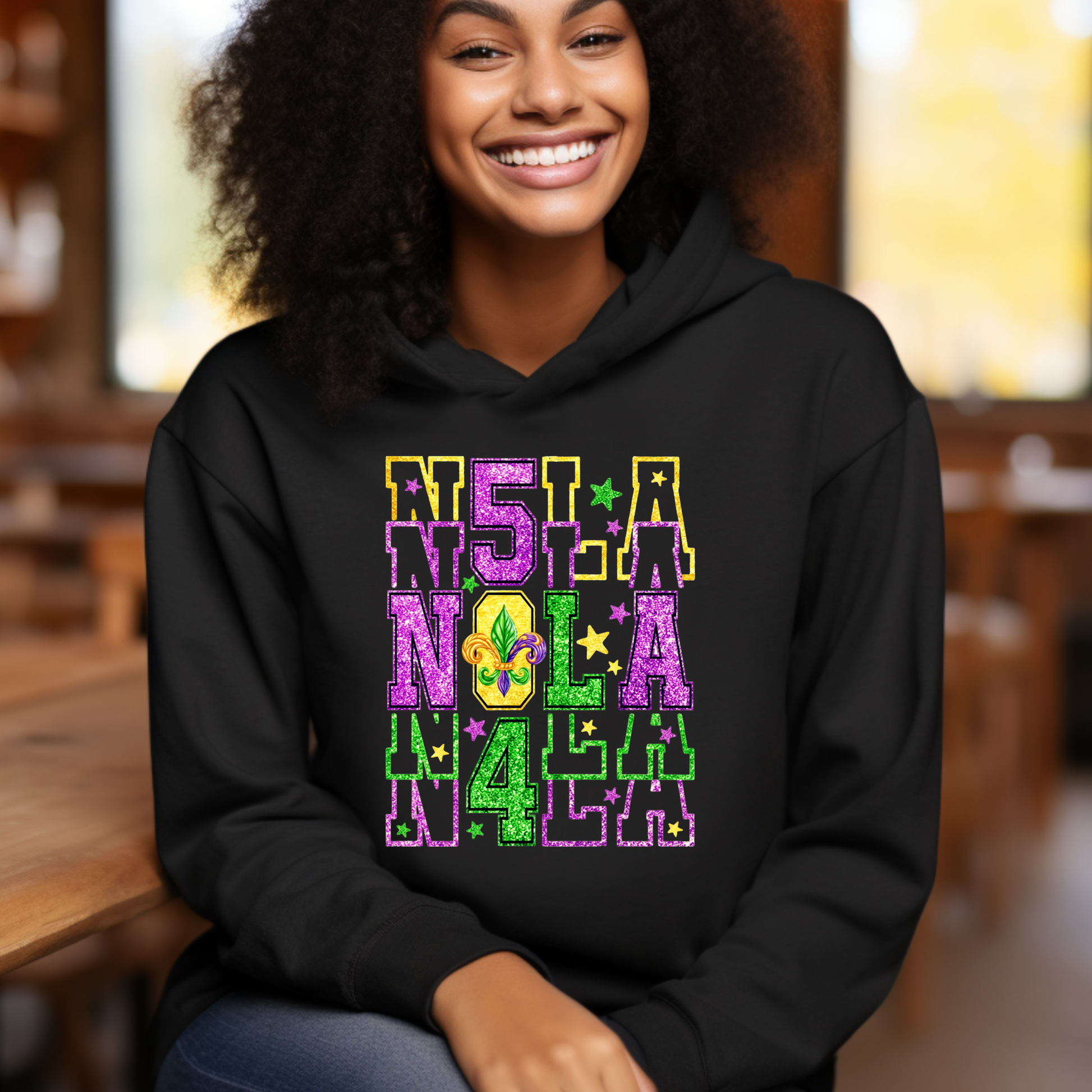 Person wearing a black hoodie with colorful 'NOLA' text and Mardi Gras elements.