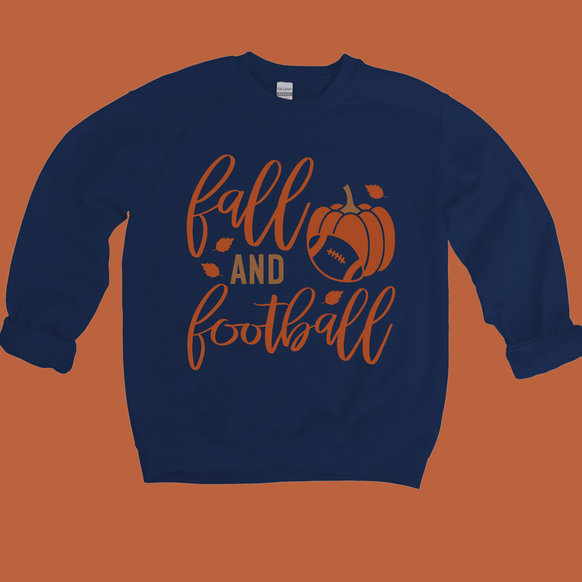 A navy blue crewneck sweatshirt with a 'fall and football' graphic in orange and brown, displayed flat against a solid orange background.