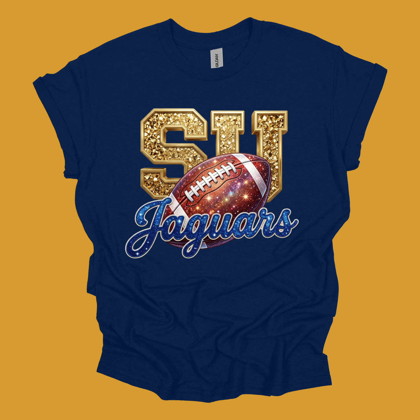 A navy blue short-sleeve t-shirt with a graphic print featuring gold glittery 'SU' letters, a football with a galaxy pattern, and 'Jaguars' in blue script, displayed against a solid mustard yellow background.