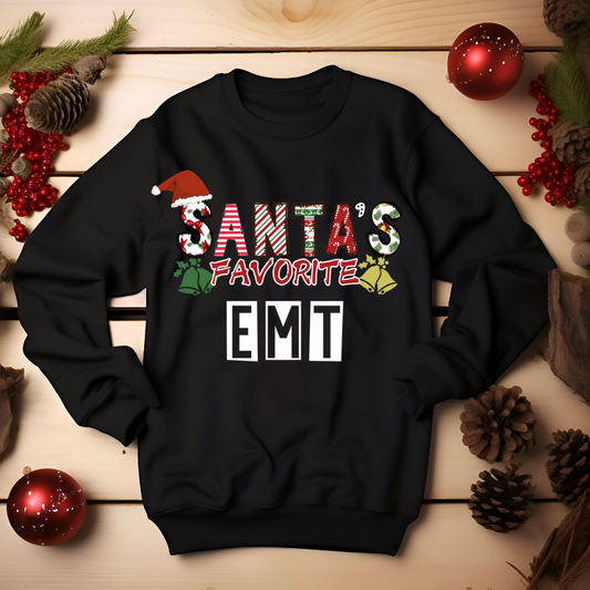 A black long-sleeve T-shirt with the text 'Santa's Favorite EMT' printed on the front, surrounded by Christmas-themed decorations like pine cones and holly berries.