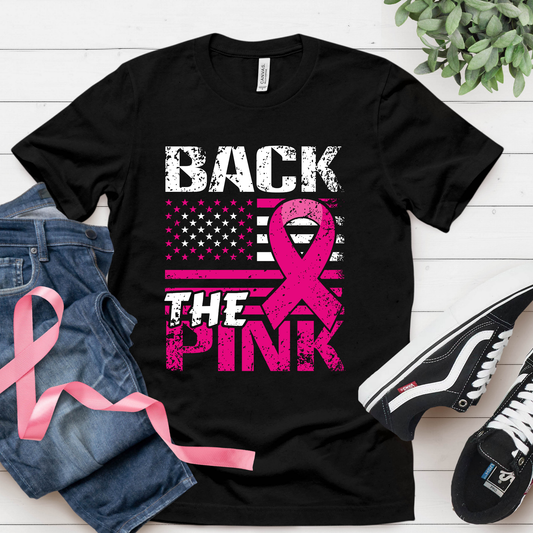 Black t-shirt with pink ribbon design and text on a white wooden surface with jeans and sneakers.
