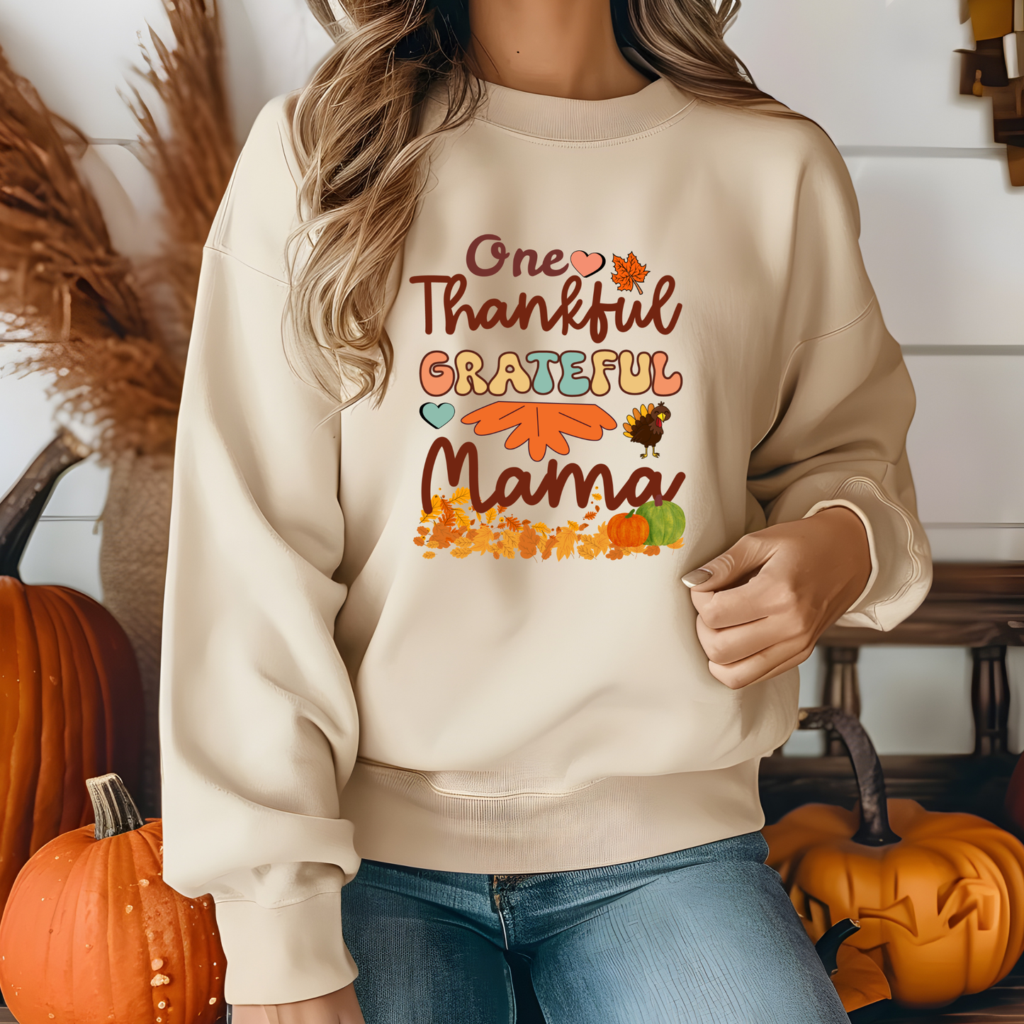 Person wearing a beige sweatshirt with 'One Thankful Grateful Mama' text and fall-themed graphics, standing in front of pumpkins.  Retro Thanksgiving Sweatshirt "One Thankful Mama" Cozy Fall Mom Crewneck