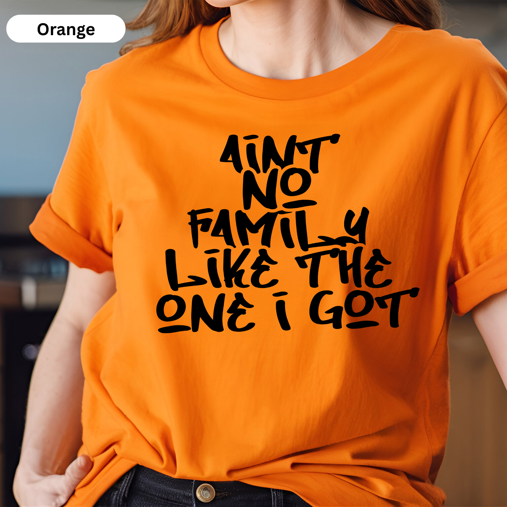 Person wearing an orange t-shirt with black text in a blurred indoor setting
