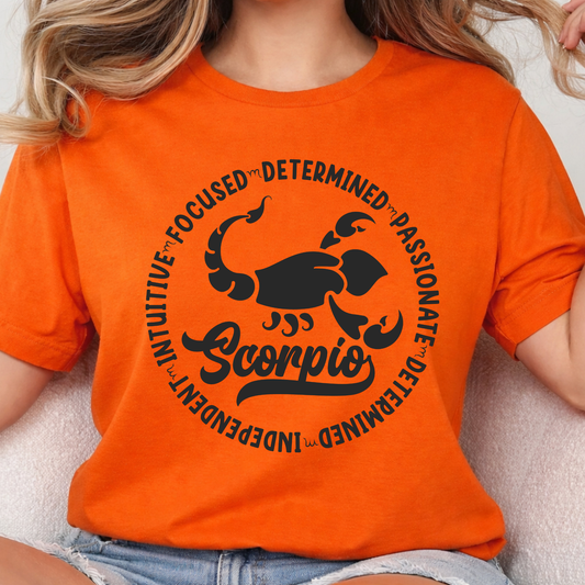 Woman wearing a orange crewneck sweatshirt featuring a white circular Scorpio zodiac graphic with a scorpion illustration, the word "Scorpio," and trait keywords like intuitive, focused, determined, passionate, and independent.