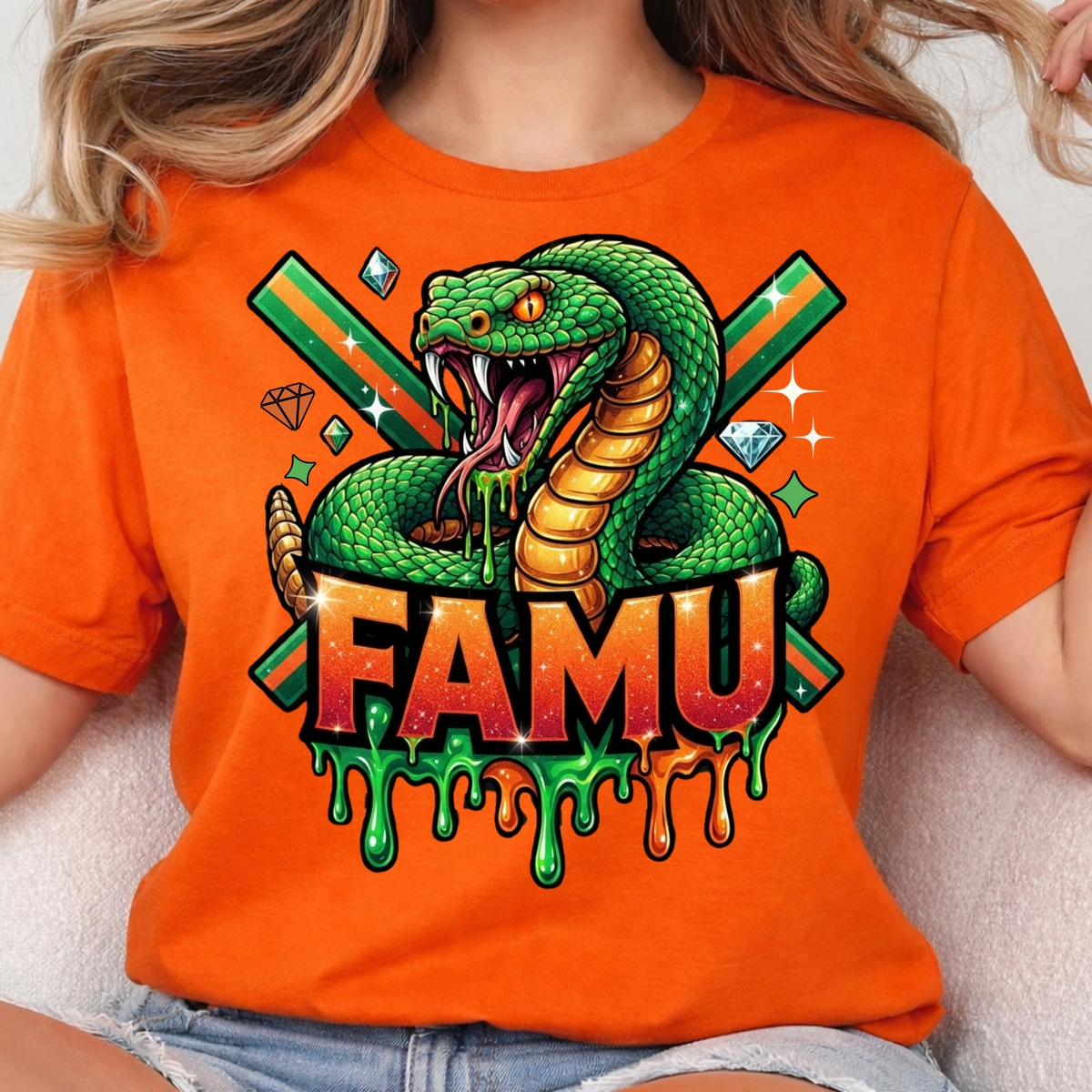 A person wearing a bright orange graphic T-shirt featuring a green coiled snake, crossed green swords, diamonds, and the word "FAMU" in dripping orange and green lettering.