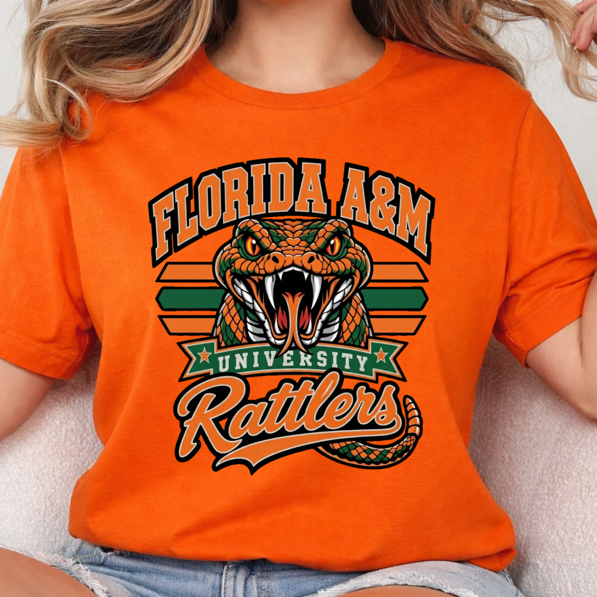 A person wearing a bright orange graphic T-shirt featuring a green coiled snake, crossed green swords, diamonds, and the word "FAMU" in dripping orange and green lettering.