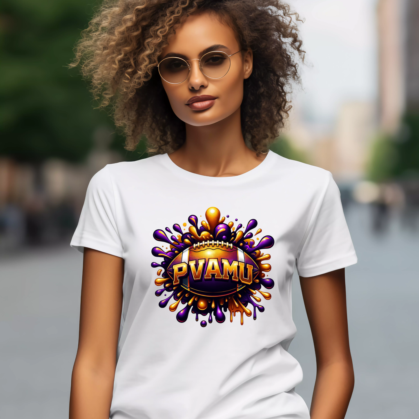 A woman with curly hair and round sunglasses wearing a white t-shirt with a colorful 'PVAMU' graphic on the chest, set against a blurred outdoor background.