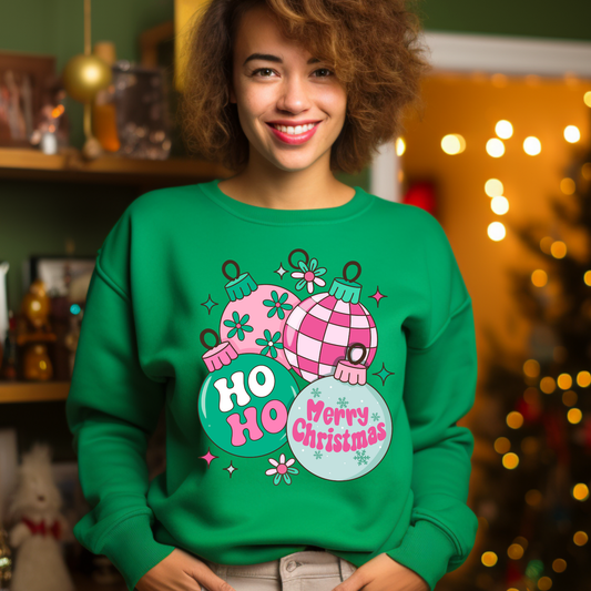 Person wearing a green 'Ho Ho Merry Christmas' sweater with festive decorations in a decorated room.