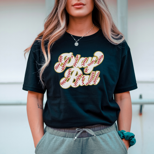 Person wearing a black t-shirt with 'Play Ball' text, standing outdoors.