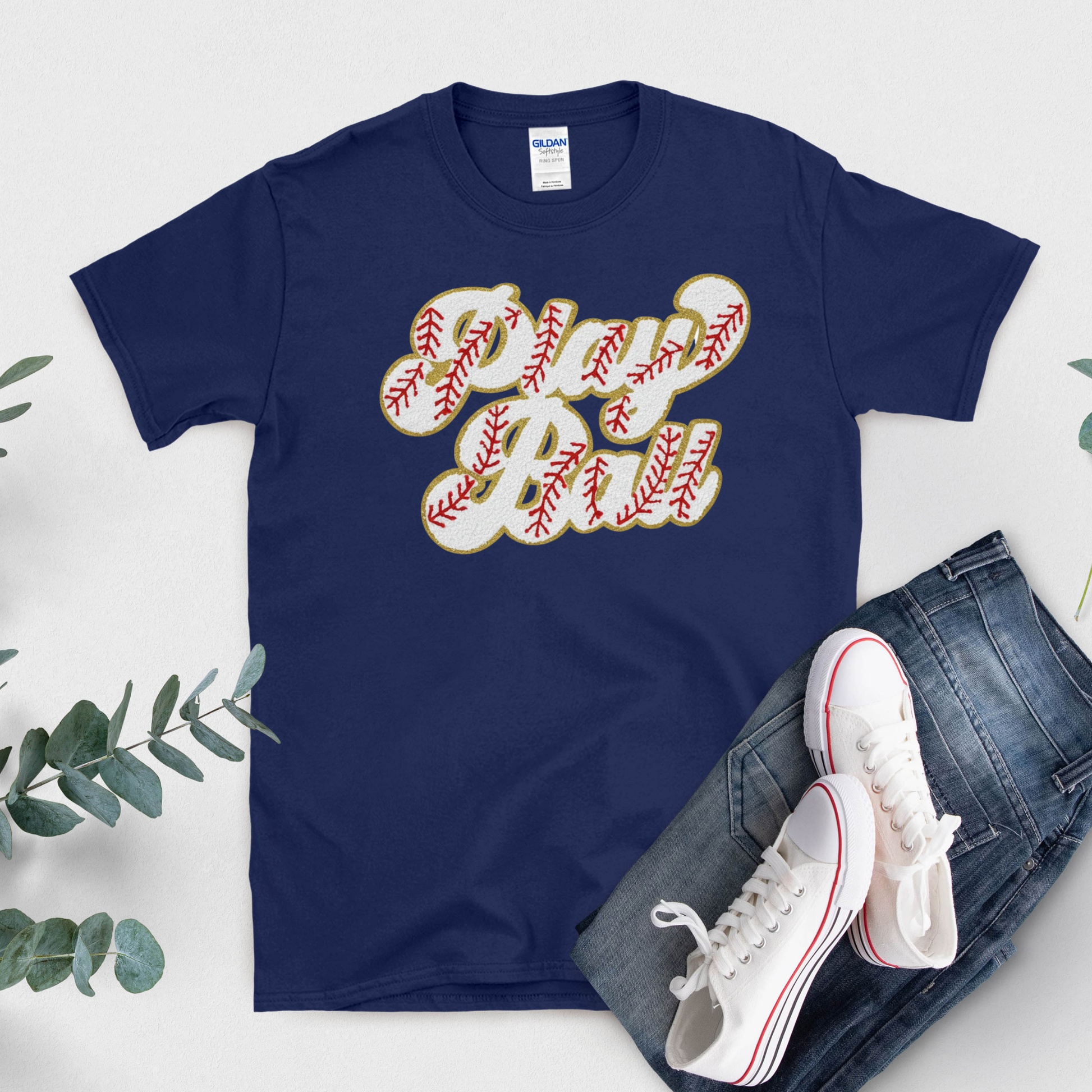 Navy blue t-shirt with 'Play Ball' design, white sneakers, and jeans on a light gray background
