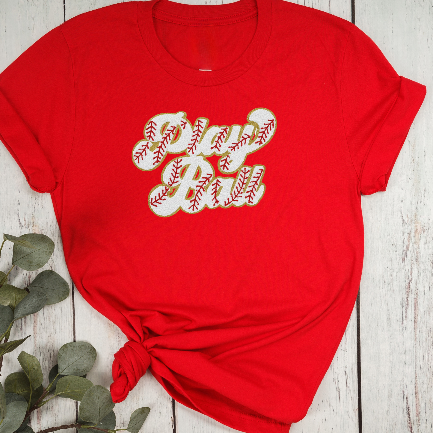 Red t-shirt with 'Baseball Girl' text on a wooden surface with greenery.