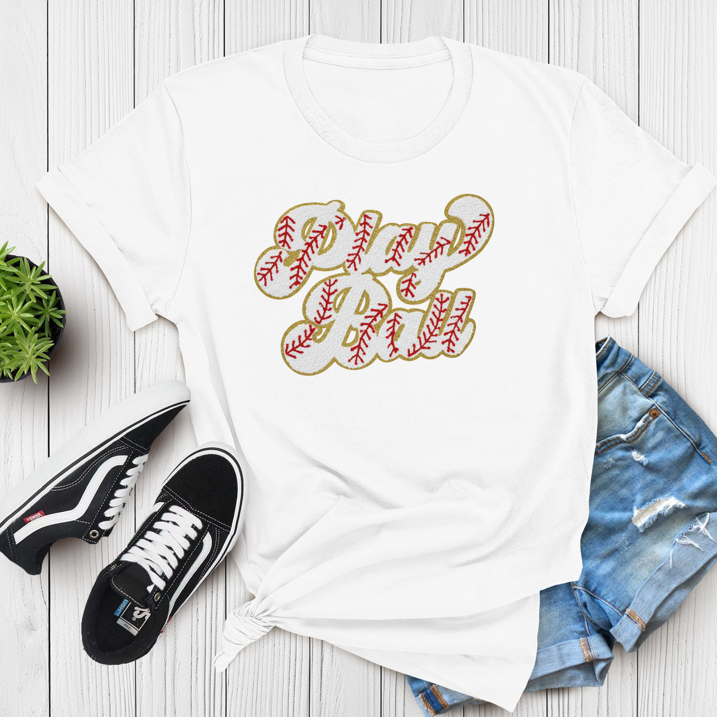 White t-shirt with 'Girl Ball' design, black sneakers, and denim shorts on a wooden surface.