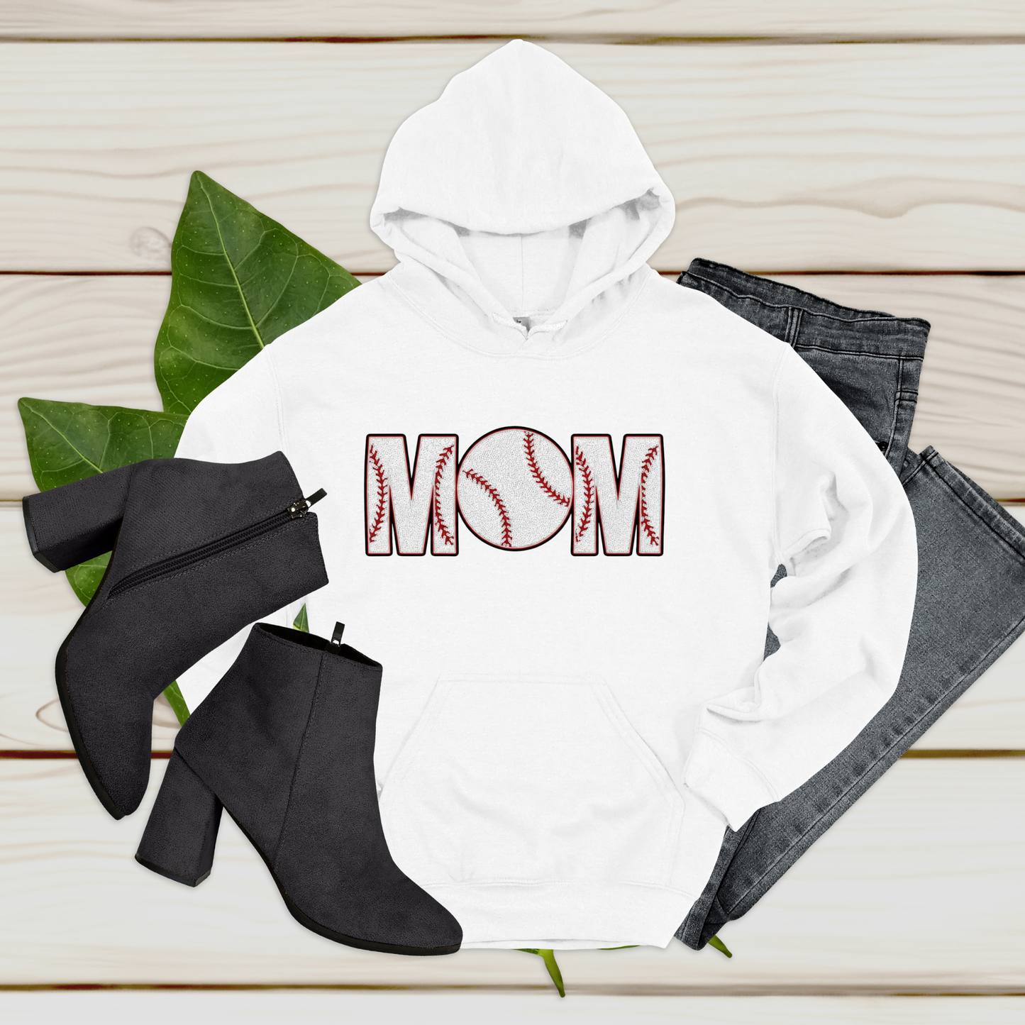 White hoodie with 'MOM' print, black boots, and jeans on a wooden surface