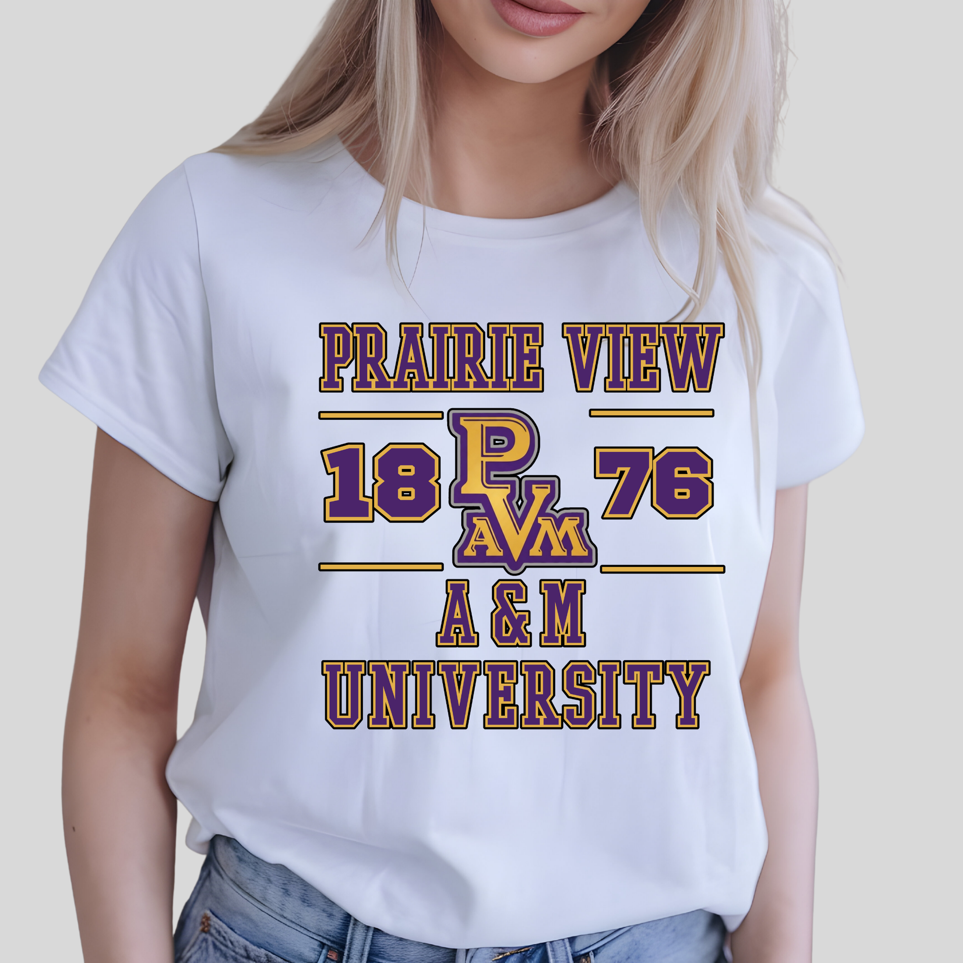 A woman wearing a white short-sleeve graphic T-shirt with 'PRAIRIE VIEW 18 PAVM 76 A&M UNIVERSITY' printed in purple and gold on the front, paired with blue jeans against a light gray background.