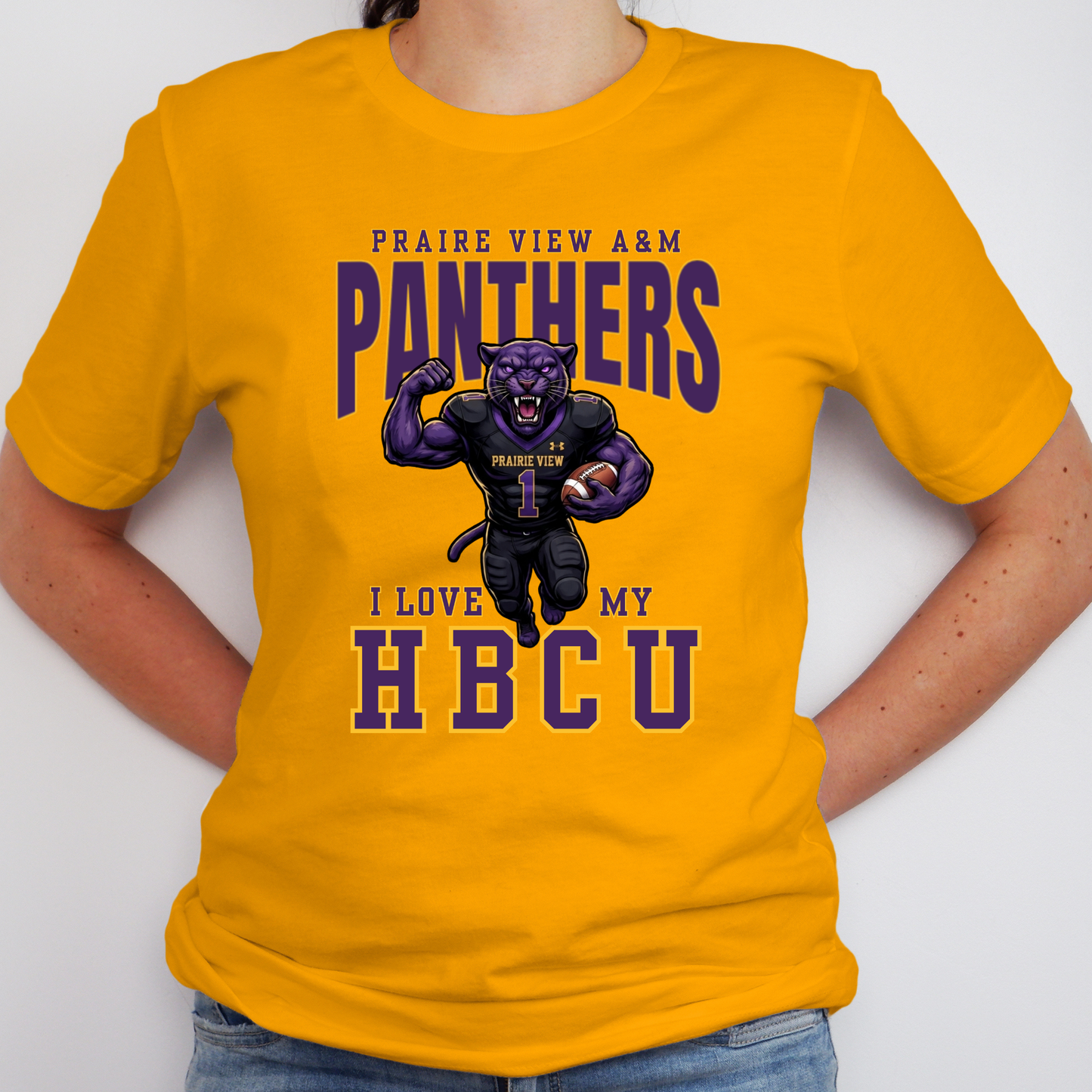 A person wearing a bright yellow graphic T-shirt with purple and navy text reading 'PRAIRE VIEW A&M PANTHERS I LOVE MY HBCU' and a cartoon panther mascot in the center, paired with blue jeans against a plain light background.