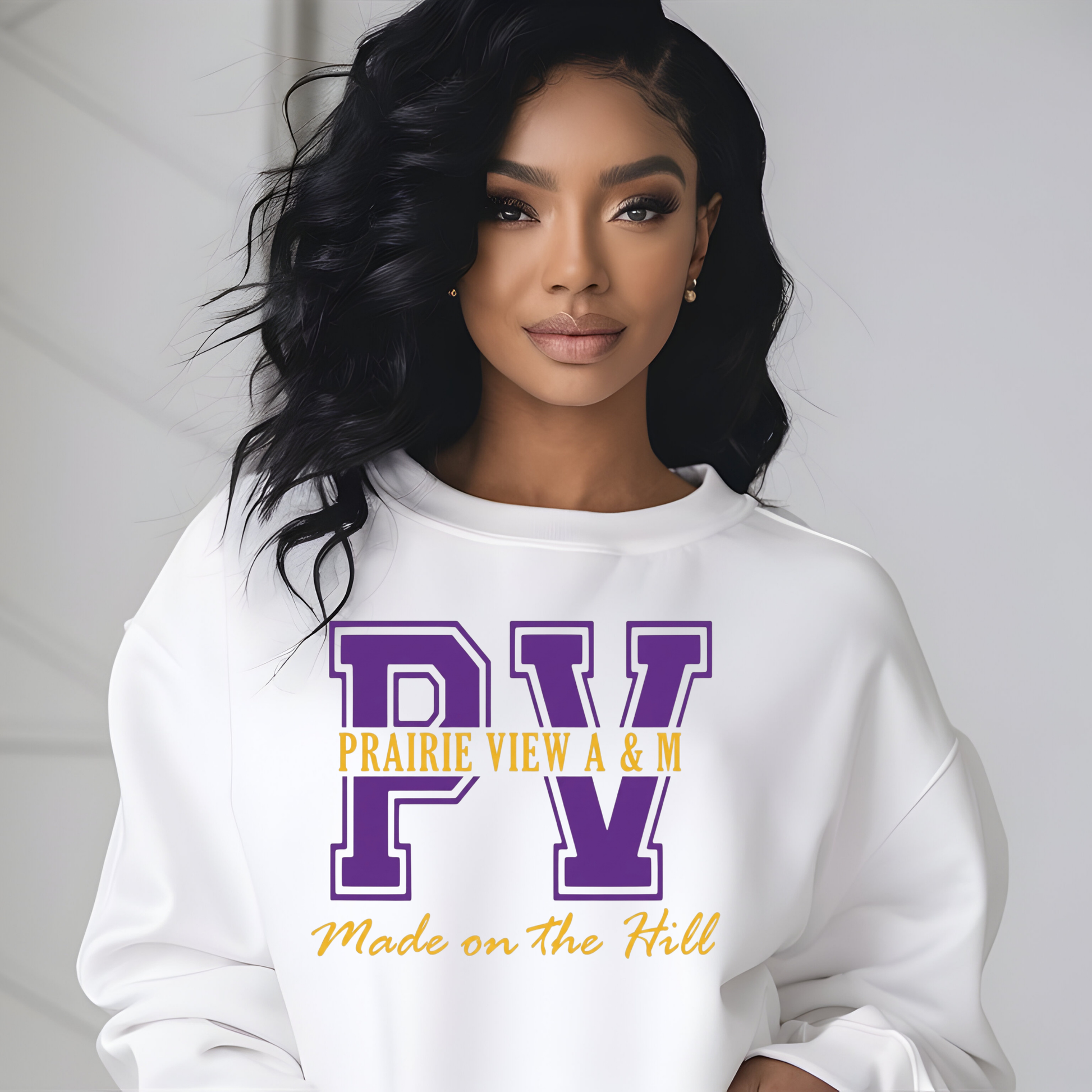 A woman with long, wavy black hair is wearing a white crewneck sweatshirt with a purple and yellow graphic on the front. The graphic features the letters 'PV' in purple, with 'PRAIRIE VIEW A & M' in yellow underneath, and 'Made on The Hill' in yellow script below.