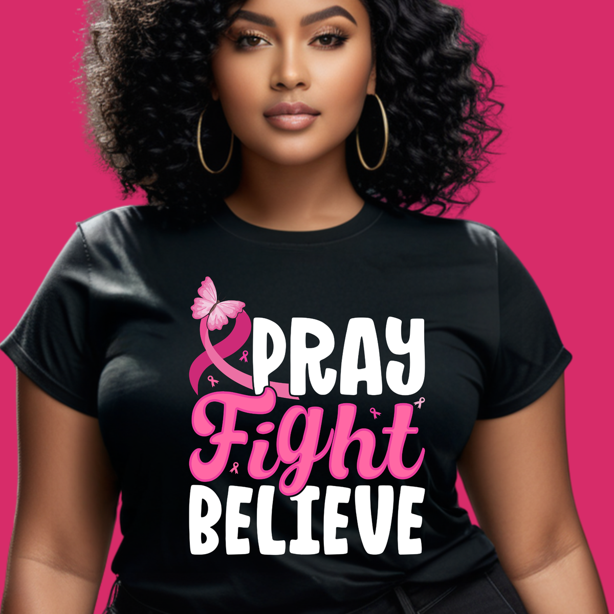 A woman with curly black hair and gold hoop earrings wears a black graphic T-shirt with the words 'PRAY Fight BELIEVE' in white and pink, alongside a pink ribbon and butterfly, against a solid pink background.