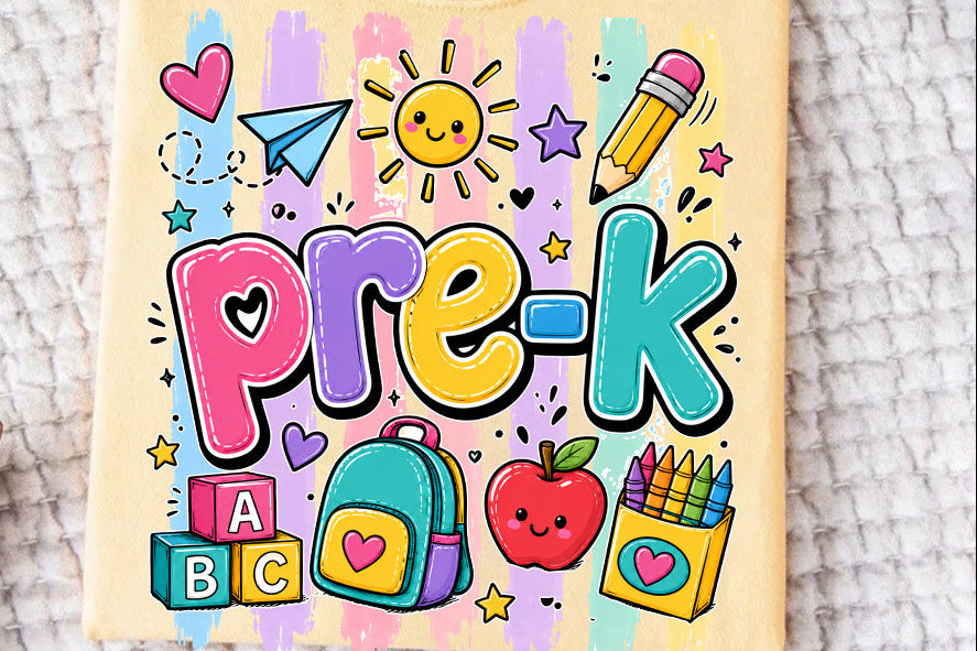 A folded pale yellow t-shirt with a colorful 'Pre-K' school supplies graphic, laid flat on a textured white blanket.