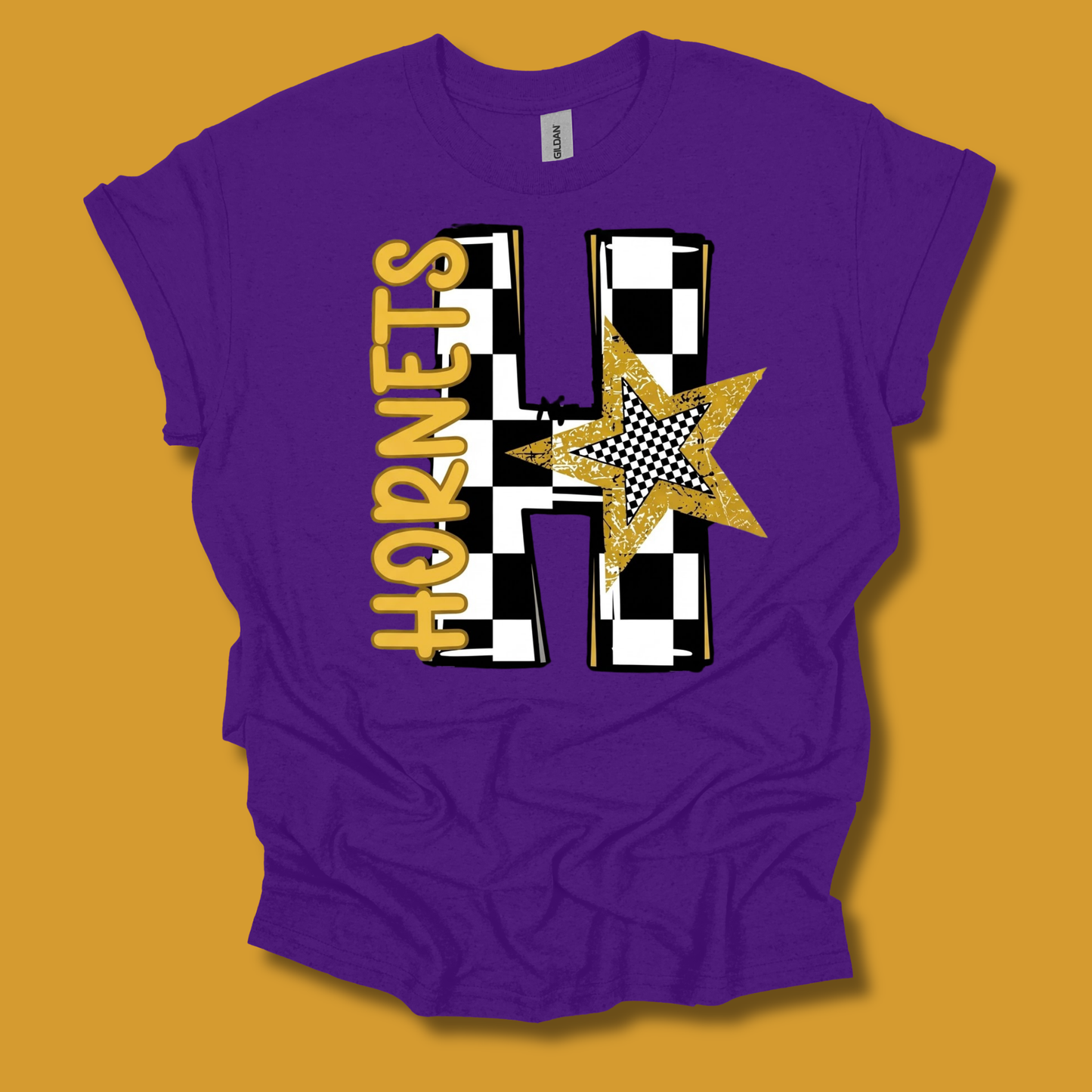 A purple short-sleeve t-shirt with a custom graphic design featuring a large black and white checkered letter 'H', the word 'HORNETS' in gold vertically, and a gold glitter star, shown on a solid mustard yellow background.