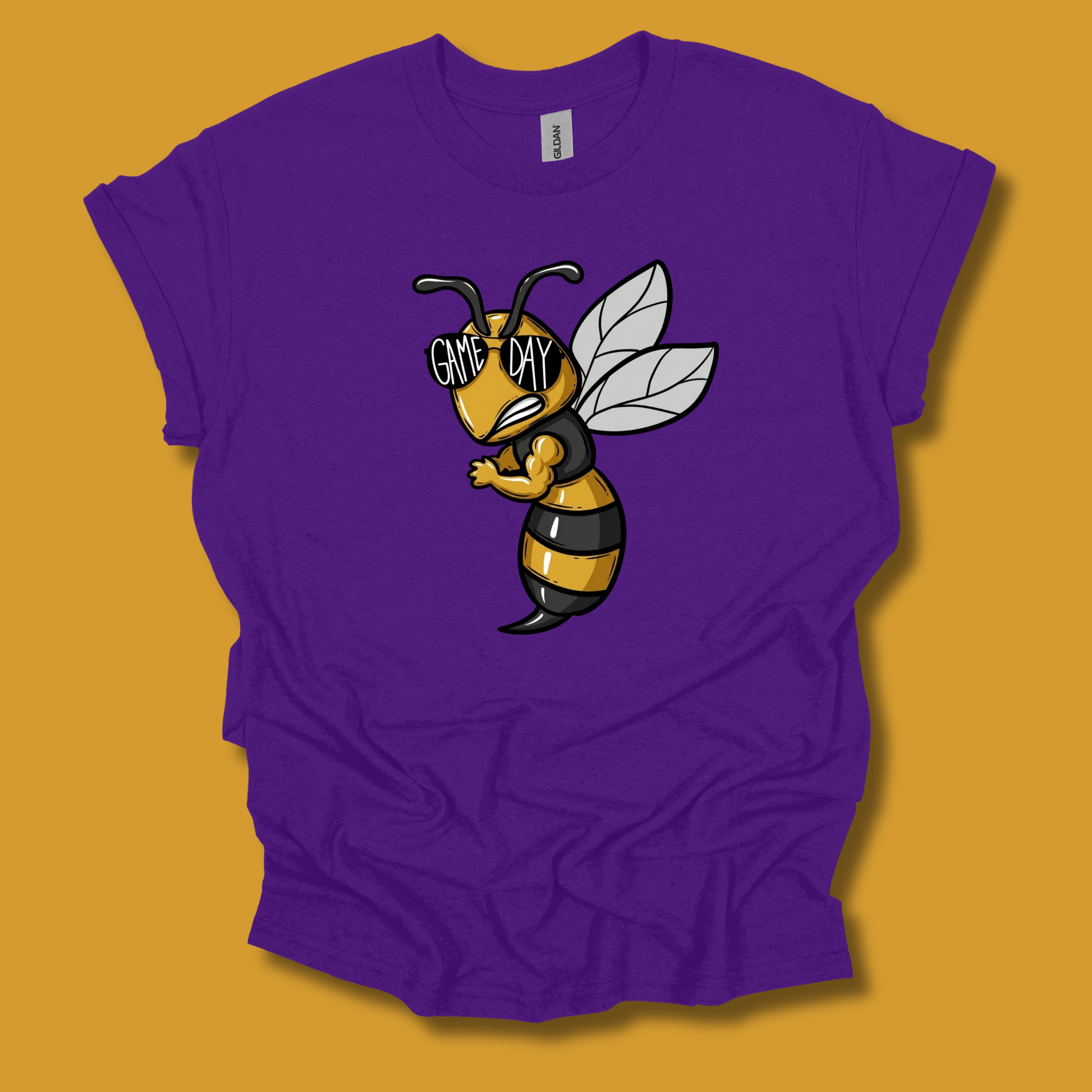 A purple short-sleeve t-shirt with a cartoon graphic of a grumpy bee wearing sunglasses that say 'GIVE ME DAY'. The shirt is displayed flat against a solid mustard yellow background.