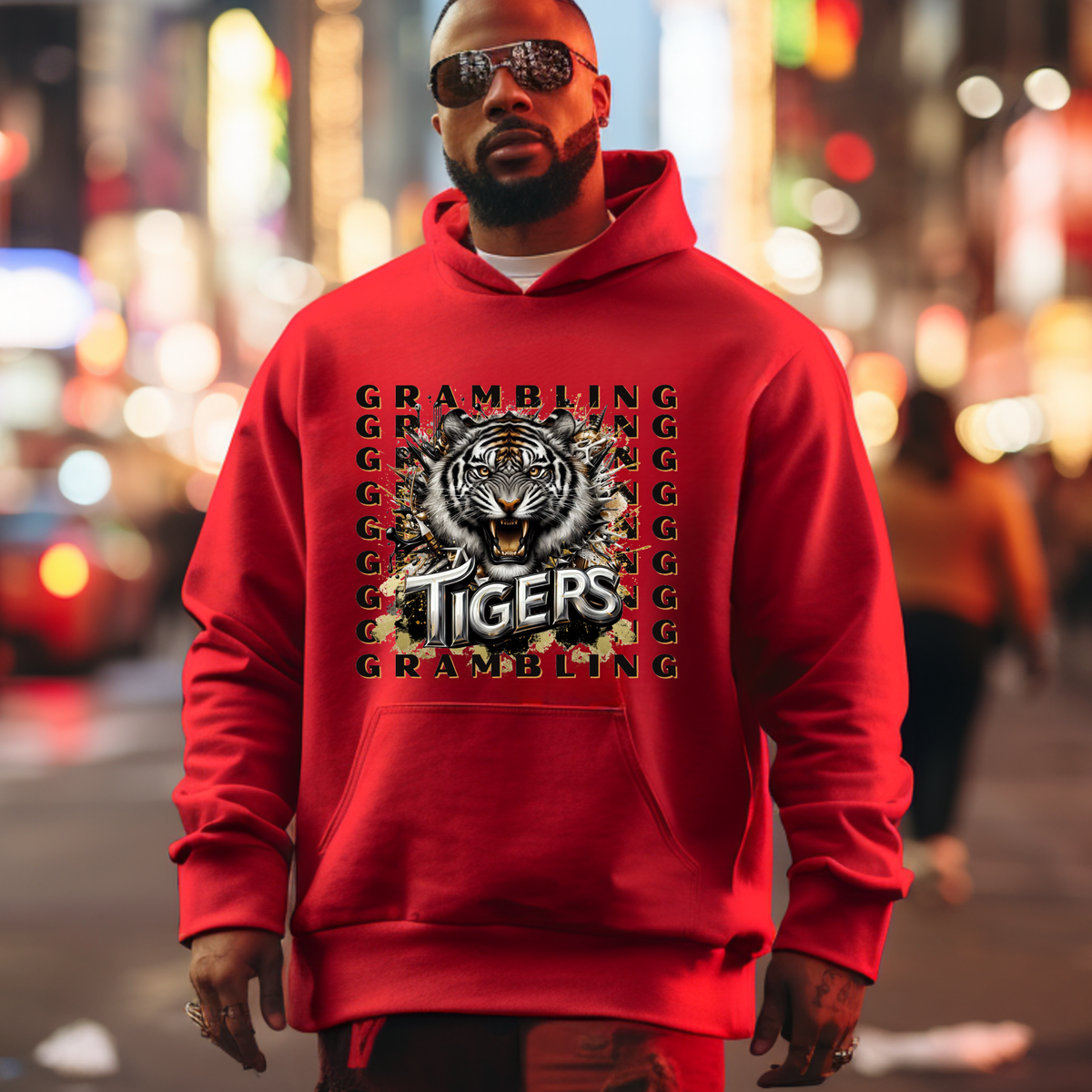 A man wearing a bright red hoodie with a large tiger graphic and the words 'GRAMBLING TIGERS' on the front, standing in a blurred city street at night.
