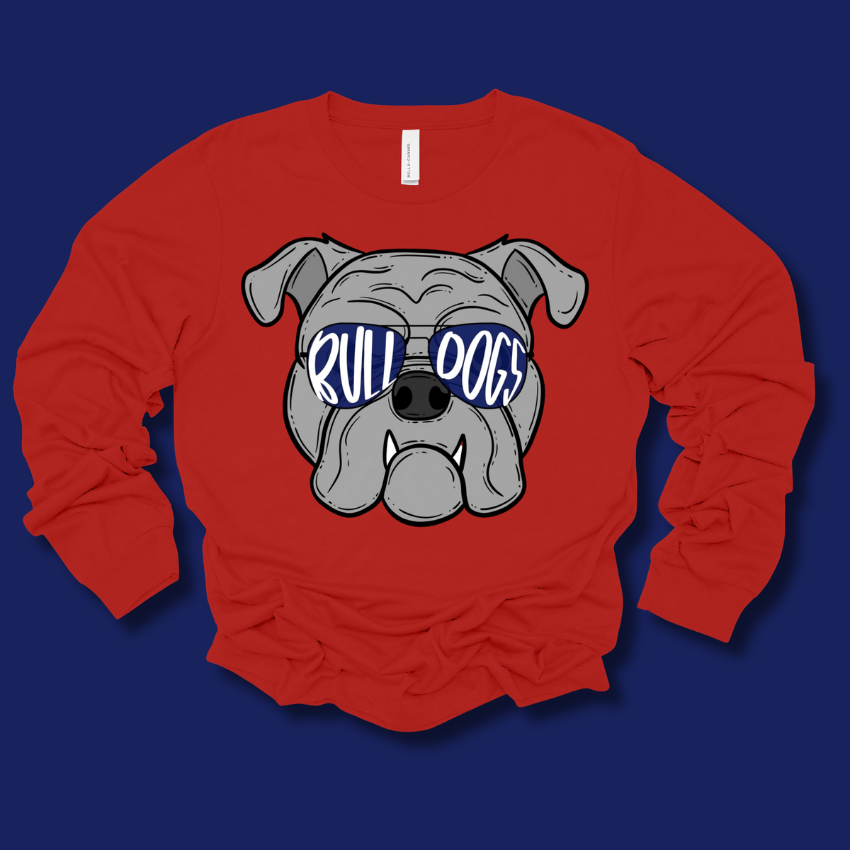 A red long-sleeve t-shirt with a cartoon bulldog graphic wearing blue sunglasses that spell out 'RULL DOGS' in white. The shirt is laid flat on a dark blue background.