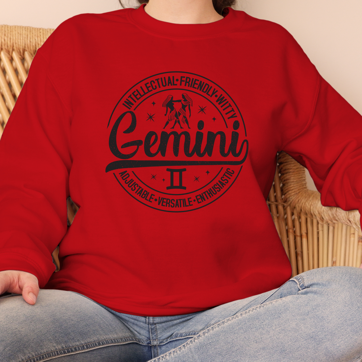 red crewneck t-shirt laid flat, featuring a circular white Gemini zodiac graphic with the twins illustration, the word "Gemini," and trait keywords like intellectual, friendly, witty, enthusiastic, versatile, and adjustable.