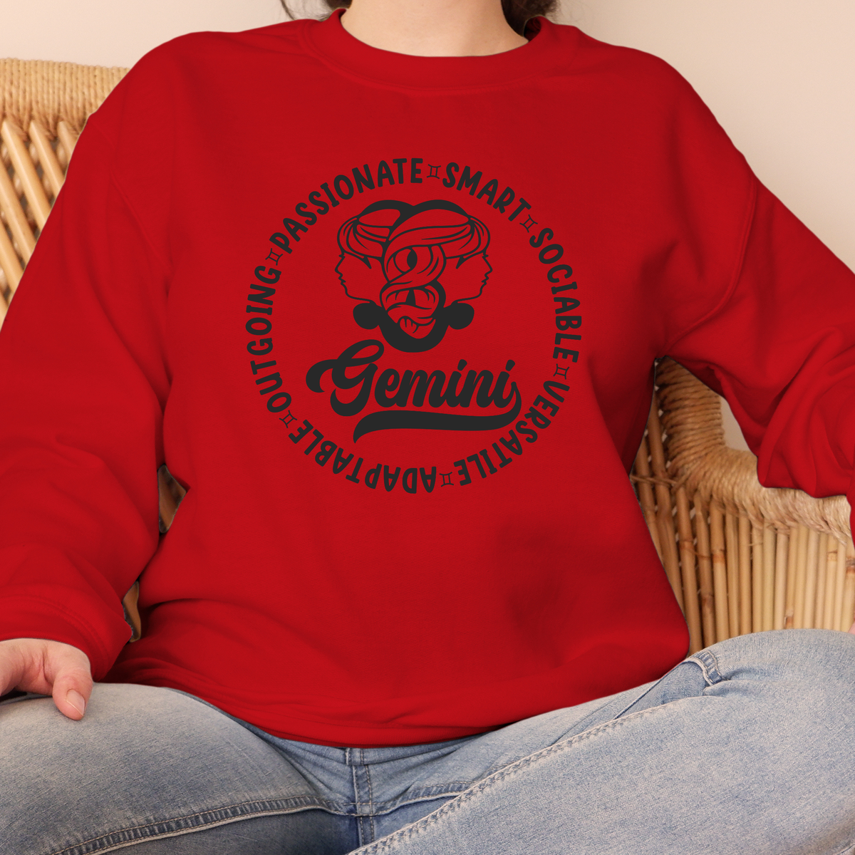 A person wearing a bright red crewneck sweatshirt with a black Libra-themed graphic on the chest, sitting on a wicker chair.