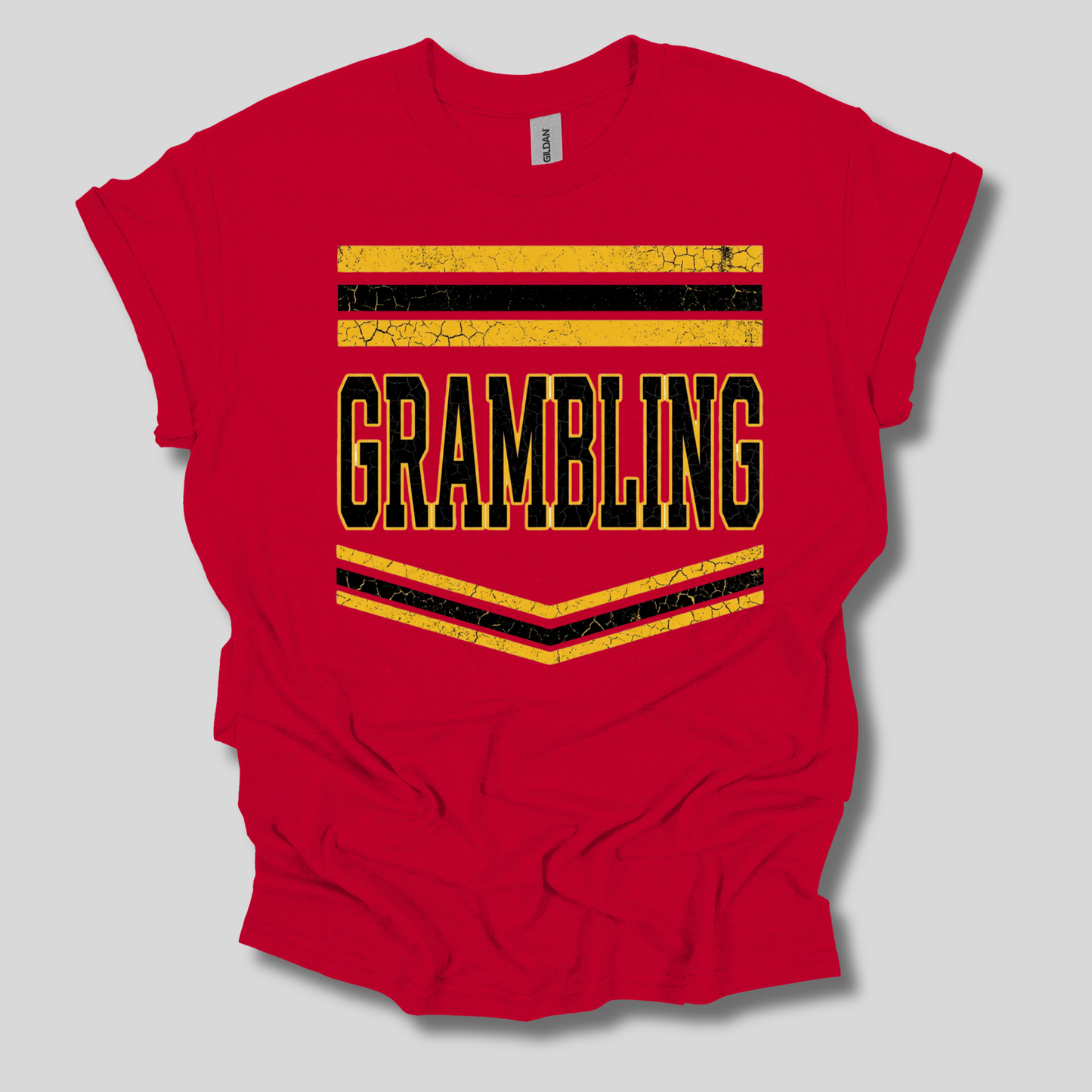 A red short-sleeve t-shirt with a distressed graphic on the front that reads 'GRAMBLING' in black letters outlined in yellow, framed by yellow and black stripes, shown on a light gray background.
