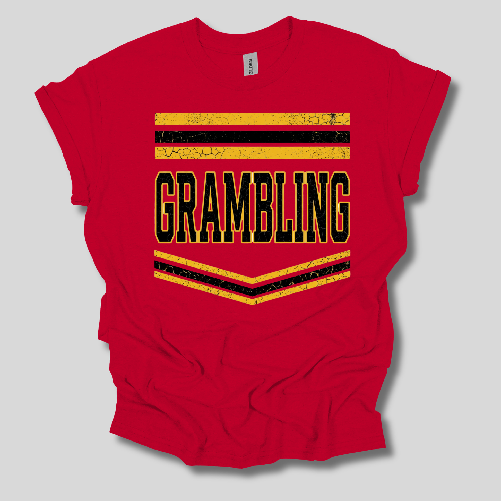 A red short-sleeve t-shirt with a distressed graphic on the front that reads 'GRAMBLING' in black letters outlined in yellow, framed by yellow and black stripes, shown on a light gray background.