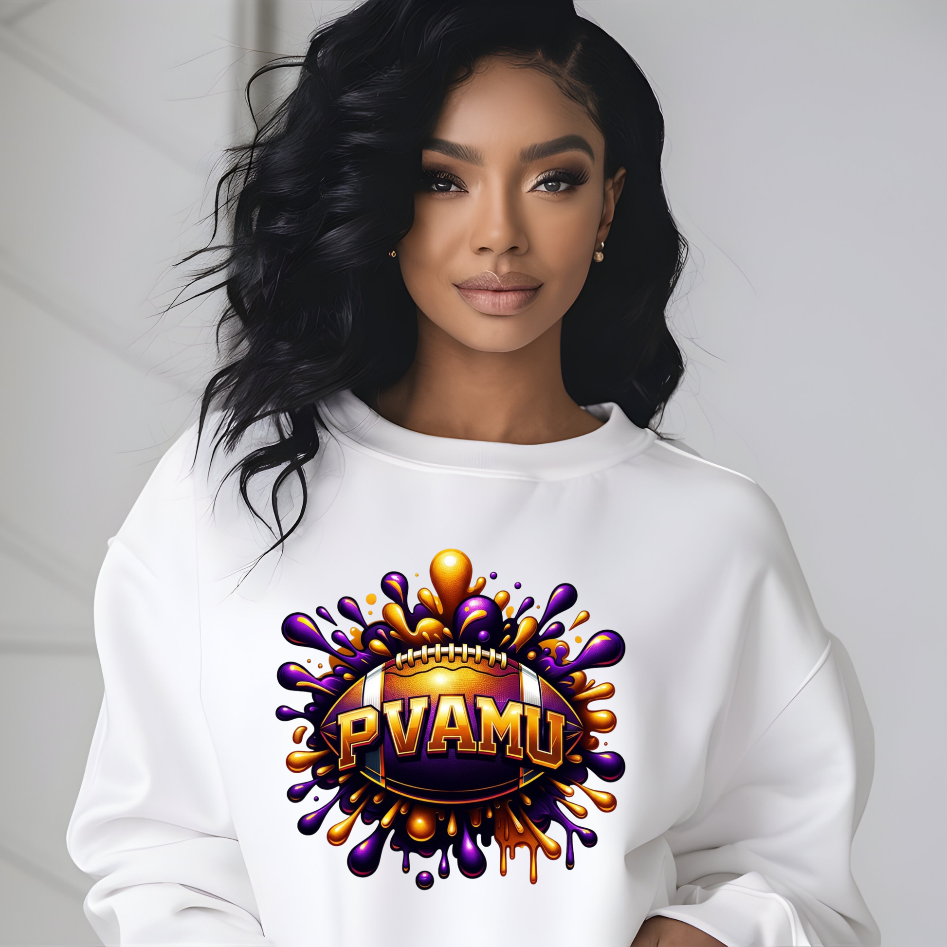 A woman wearing a white crewneck sweatshirt with a colorful graphic print on the front. The graphic features a football-shaped badge with the text 'PVAMU' in gold, surrounded by purple and orange paint splatters.