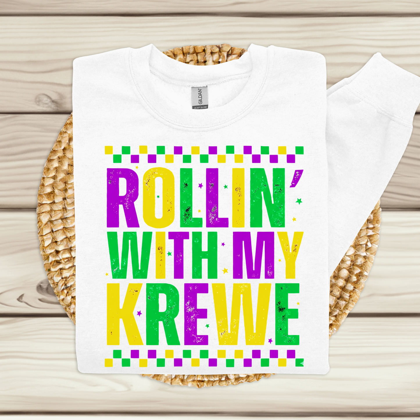 White t-shirt with colorful text 'Rollin' with my Krewe' on a woven mat.