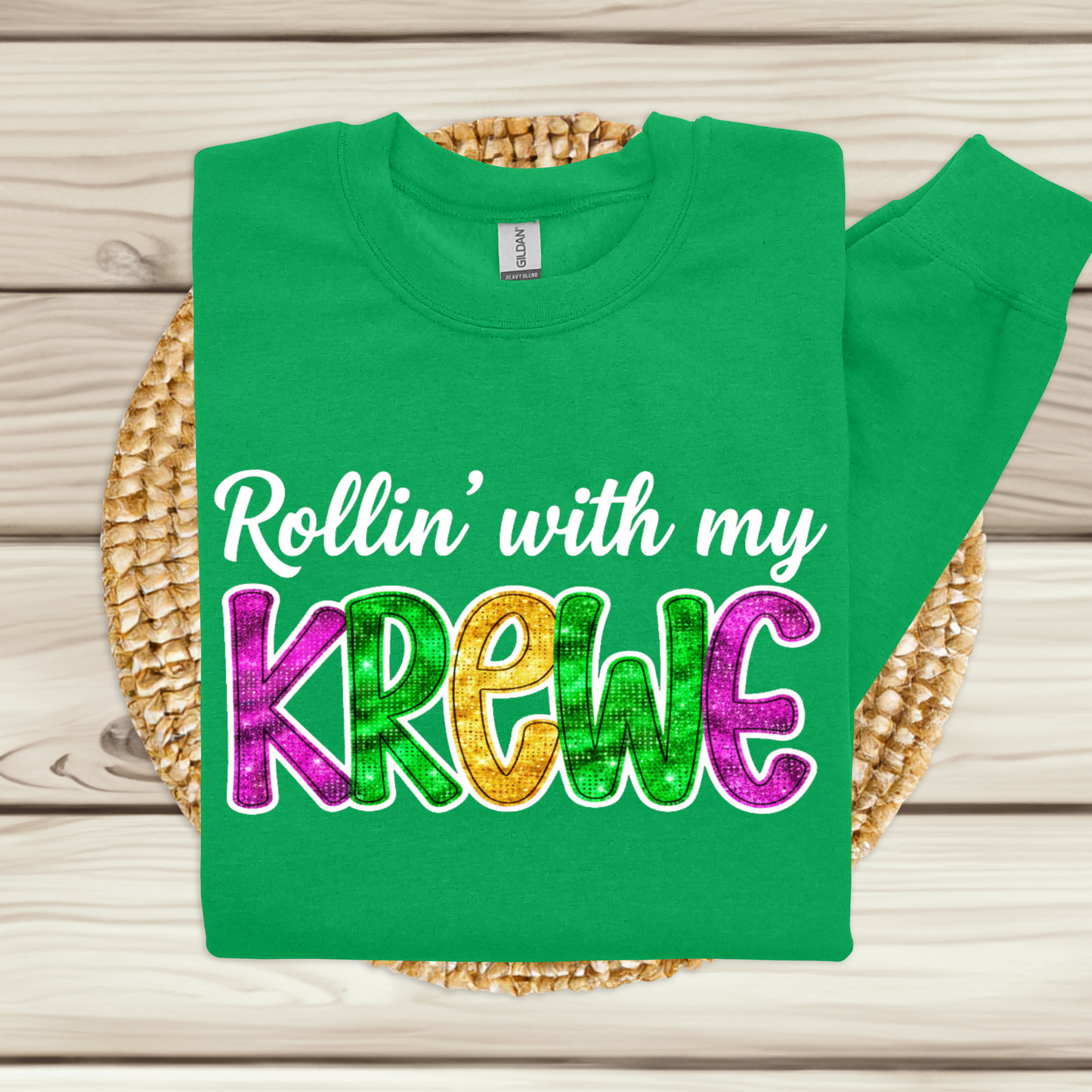 Green t-shirt with colorful text 'Rollin' with my Krewe' on a woven mat.