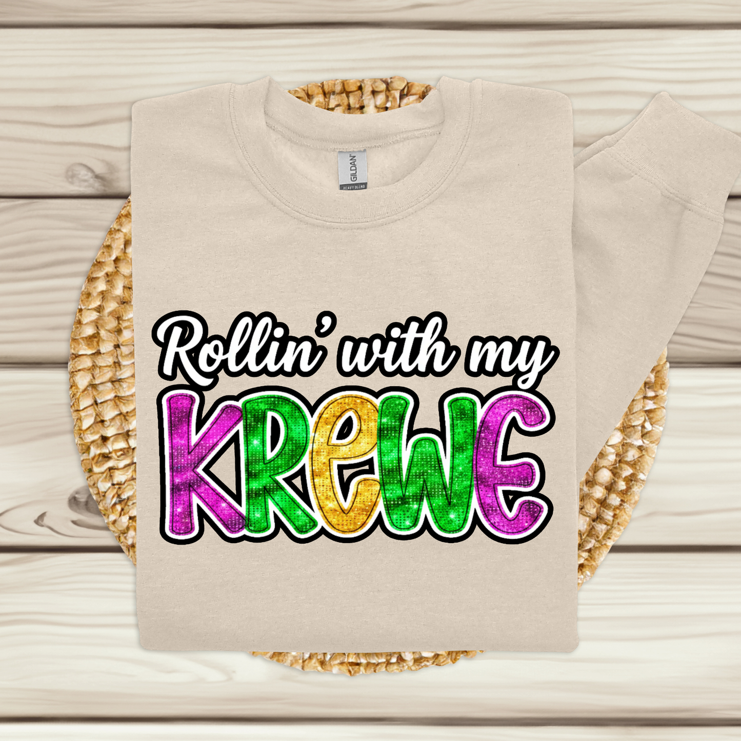 Beige t-shirt with colorful text 'Rollin' with my Krewe' on a wooden surface