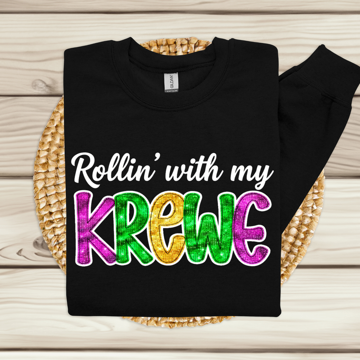 Black sweatshirt with colorful text 'Rollin' with my Krewe' on a woven mat.