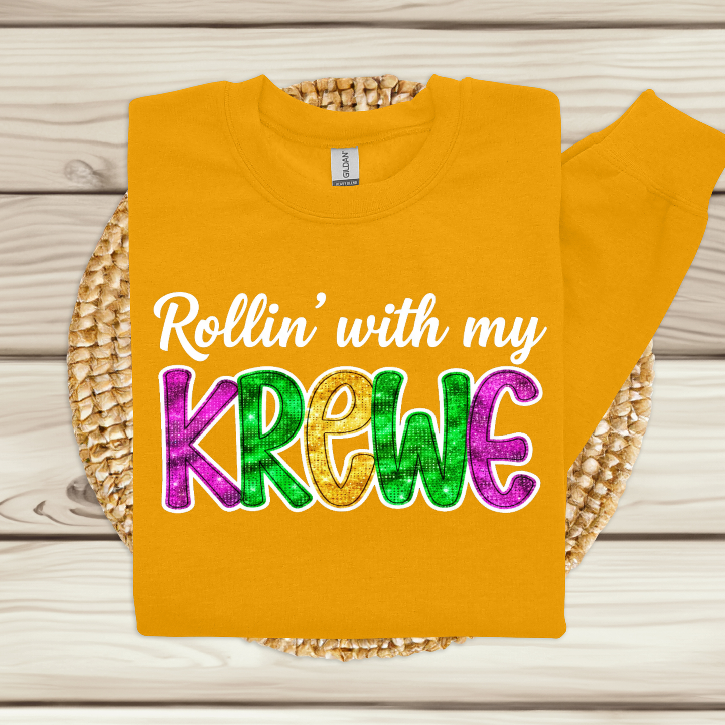 Yellow t-shirt with colorful text 'Rollin' with my Krewe' on a wooden surface