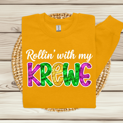 Yellow t-shirt with colorful text 'Rollin' with my Krewe' on a wooden surface