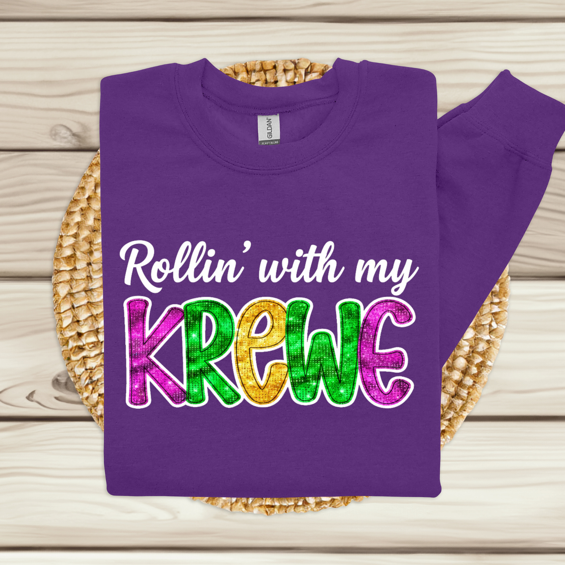 Purple sweatshirt with colorful text 'Rollin' with my Krewe' on a wooden surface