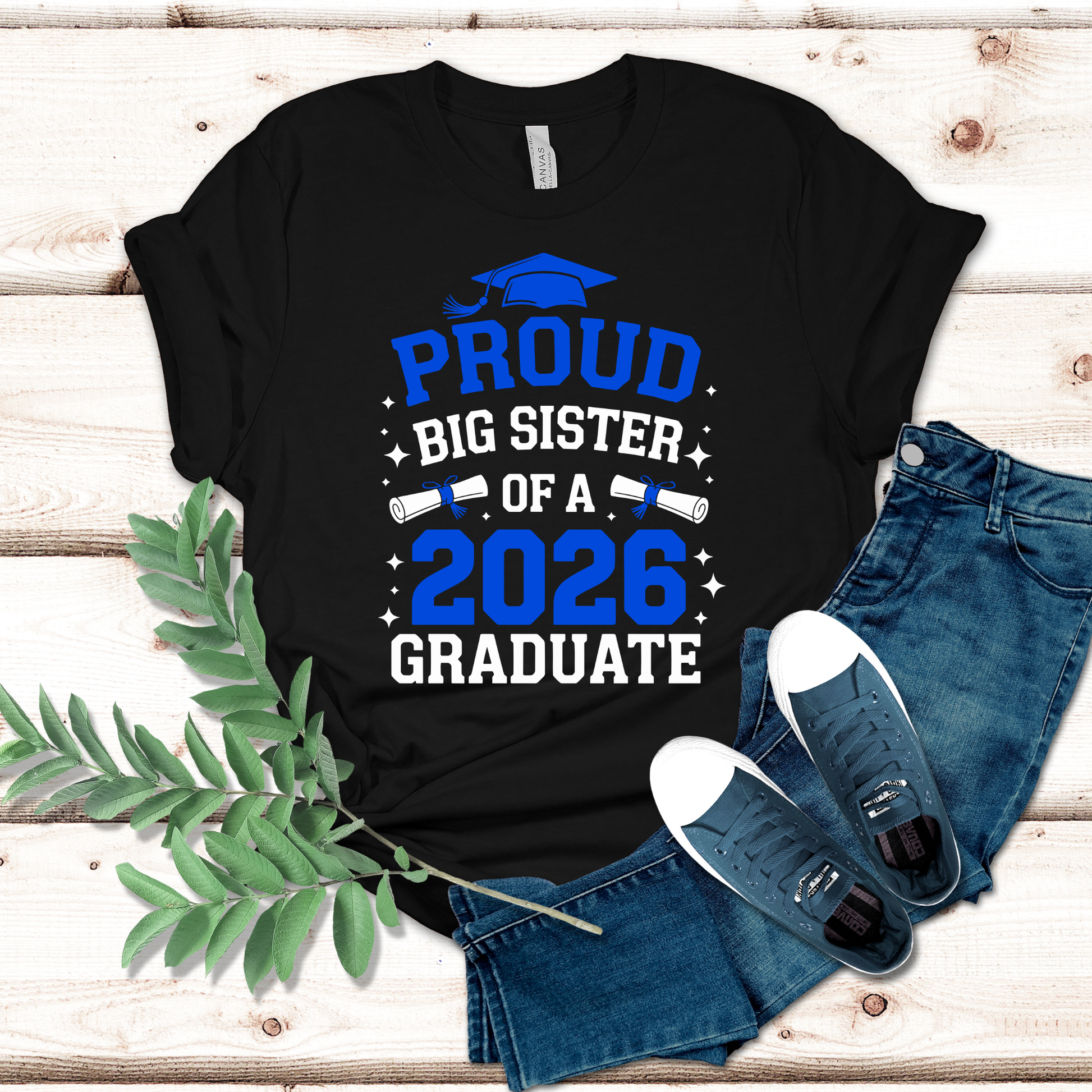 Black t-shirt with 'Proud Big Sister of a 2026 Graduate' text on a wooden surface with jeans and shoes.
