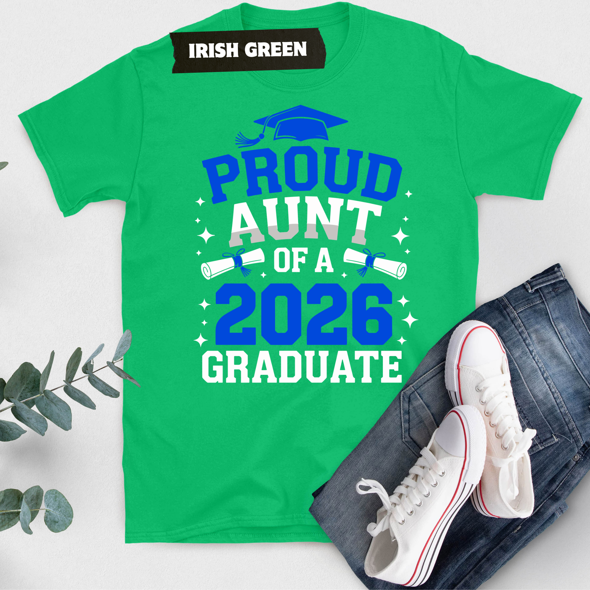 Green t-shirt with 'Proud Aunt of a 2026 Graduate' text, white sneakers, and jeans on a light gray background.