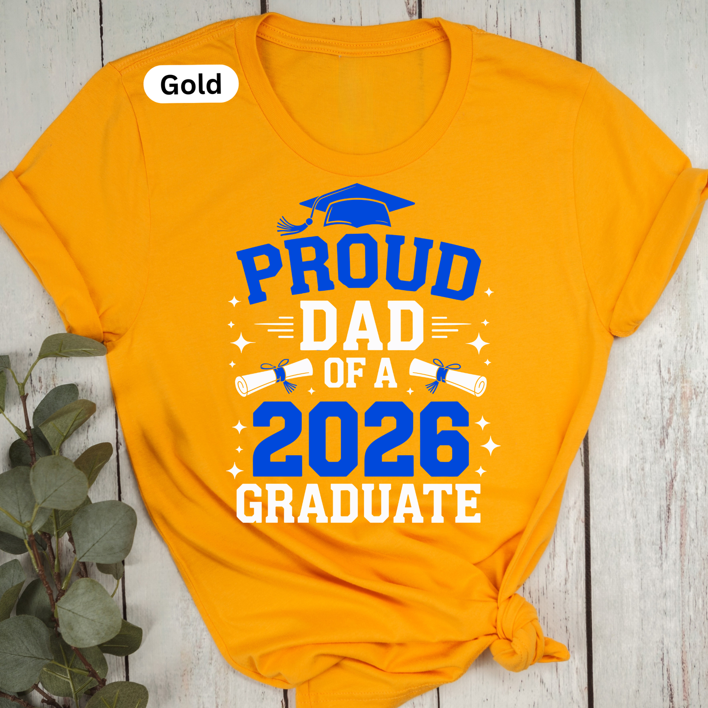Orange t-shirt with 'Proud Dad of a 2026 Graduate' text on a wooden surface.