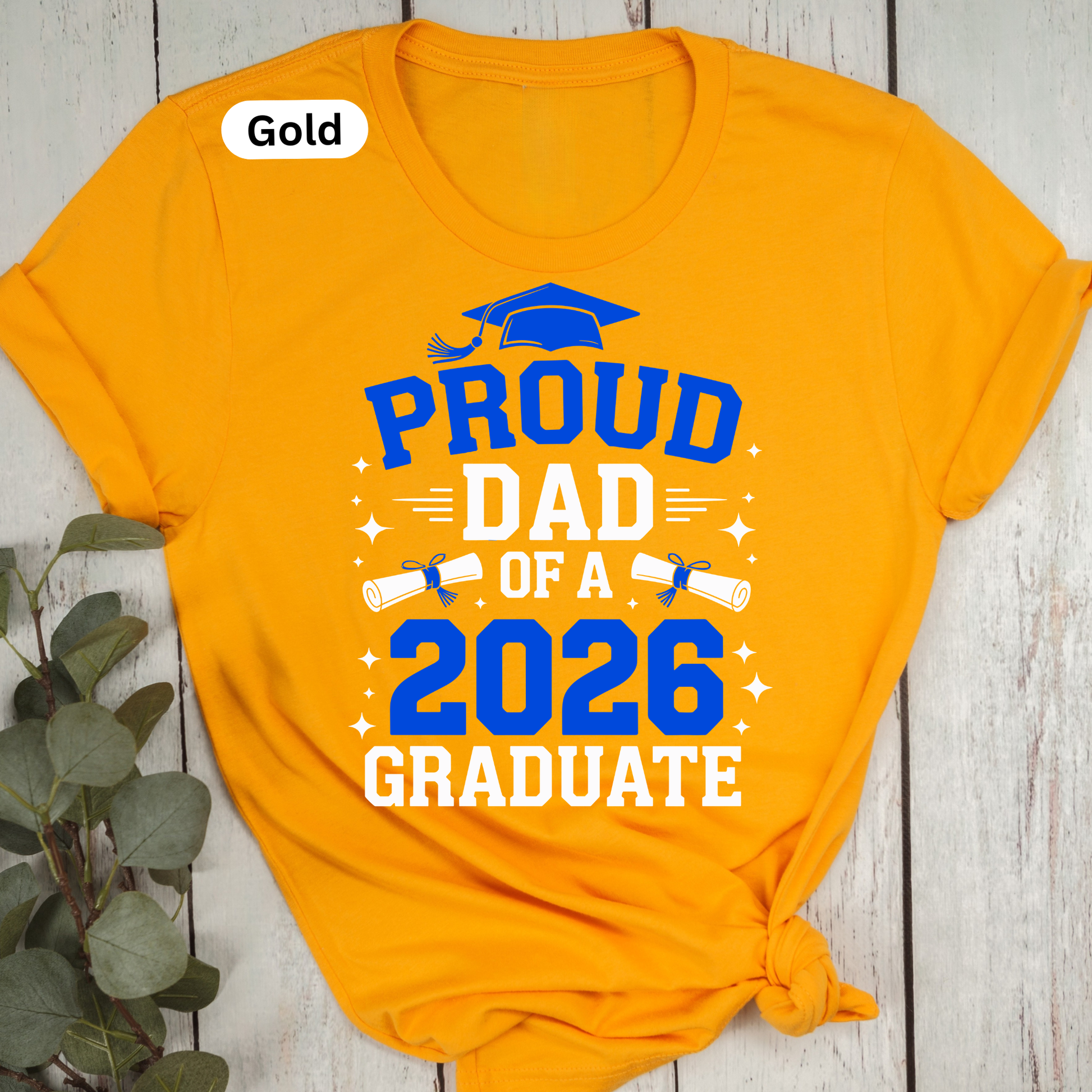 Orange t-shirt with 'Proud Dad of a 2026 Graduate' text on a wooden surface.