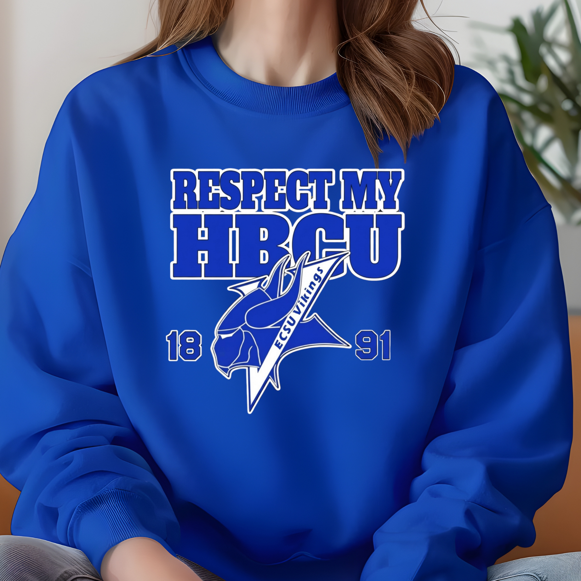 A person wearing a royal blue crewneck sweatshirt with a white and blue graphic that reads 'RESPECT MY HBCU' and includes a horse mascot and 'COWBOYS' text, photographed indoors with a blurred background.