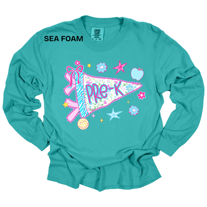 A turquoise long-sleeve t-shirt with a colorful 'Pre-K' pennant graphic on the front, featuring a ribbon, stars, and flowers. The text 'SEA FOAM' is printed in black near the upper left chest.