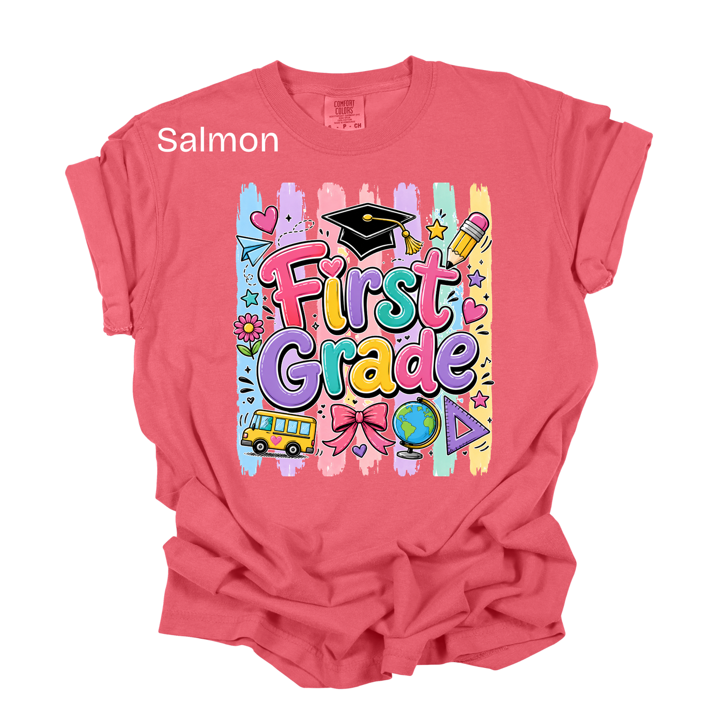 A salmon pink short-sleeve t-shirt with a colorful 'First Grade' graphic on the front, featuring school-themed doodles like a graduation cap, pencil, globe, and bus. The word 'Salmon' is printed in white text near the upper left chest.