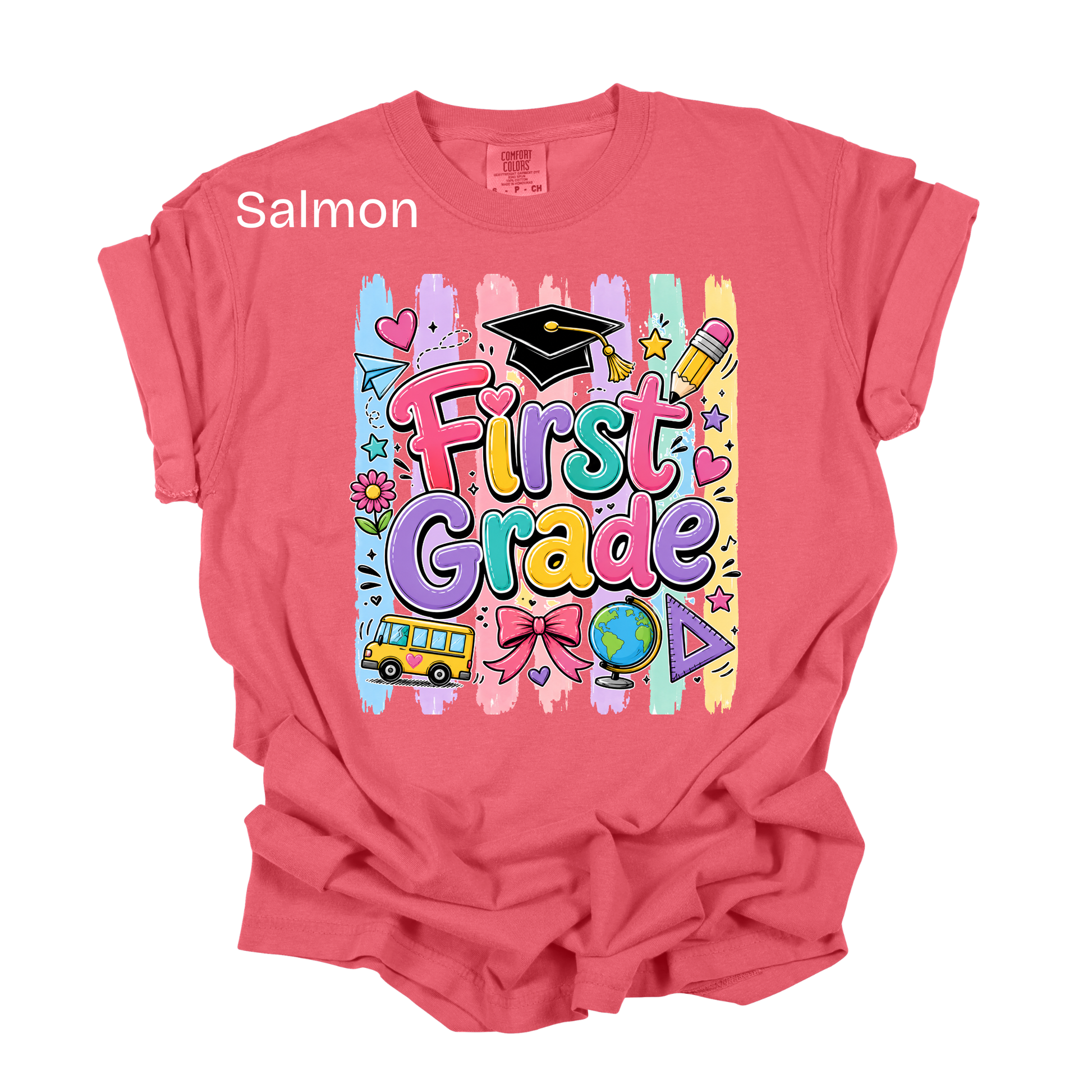 A salmon pink short-sleeve t-shirt with a colorful 'First Grade' graphic on the front, featuring school-themed doodles like a graduation cap, pencil, globe, and bus. The word 'Salmon' is printed in white text near the upper left chest.