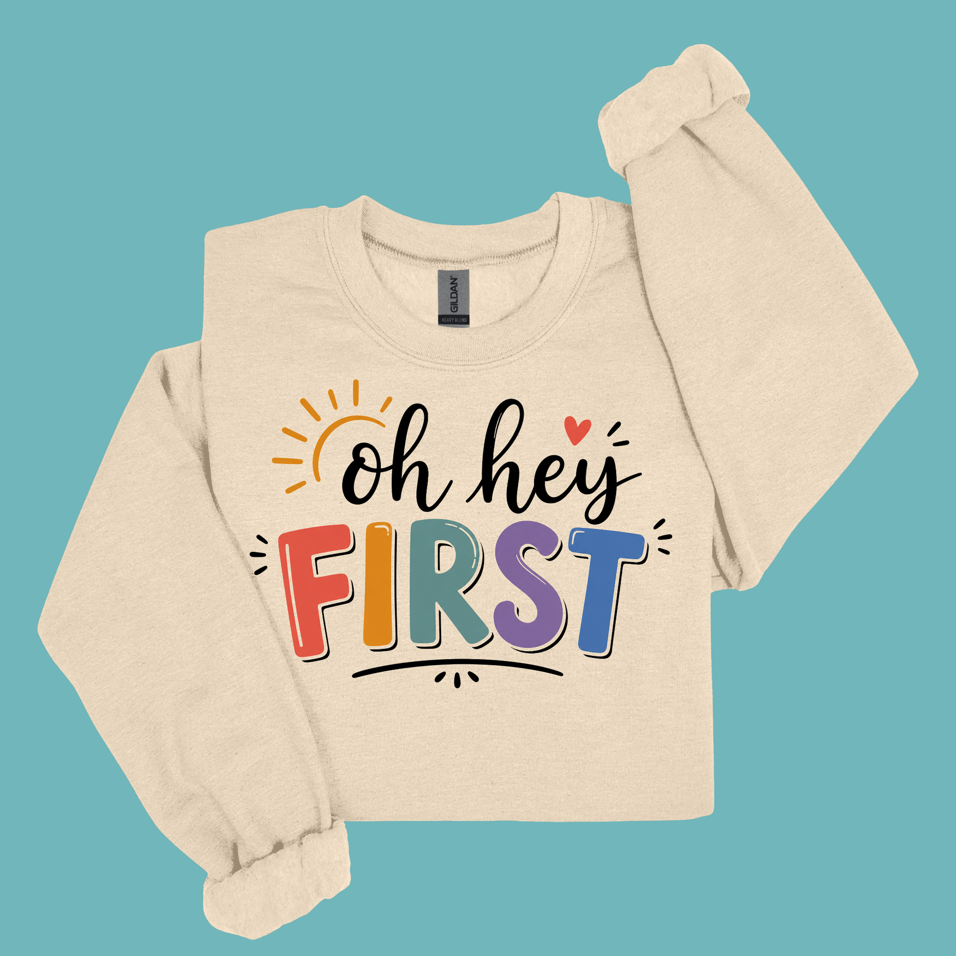 A beige long-sleeve sweatshirt with a colorful graphic reading 'Kinder Garten' in decorative letters, surrounded by small Easter-themed illustrations and a pink bow, shown on a solid teal background.