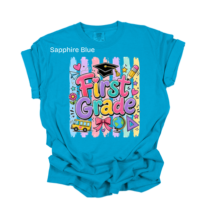 A bright blue short-sleeve t-shirt with a 'SECOND GRADE' graphic on the front, featuring a white scroll, black text, a pink bow, and a yellow pencil. The text 'Sapphire Blue' is printed on the upper left chest.