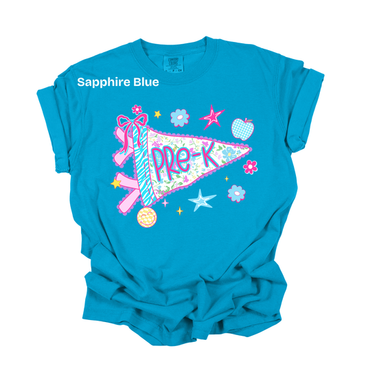 A bright turquoise blue t-shirt with a graphic of a pastel pennant flag reading 'pre-K' surrounded by stars, flowers, and a pink ribbon. The text 'Sapphire Blue' is printed on the upper left chest.