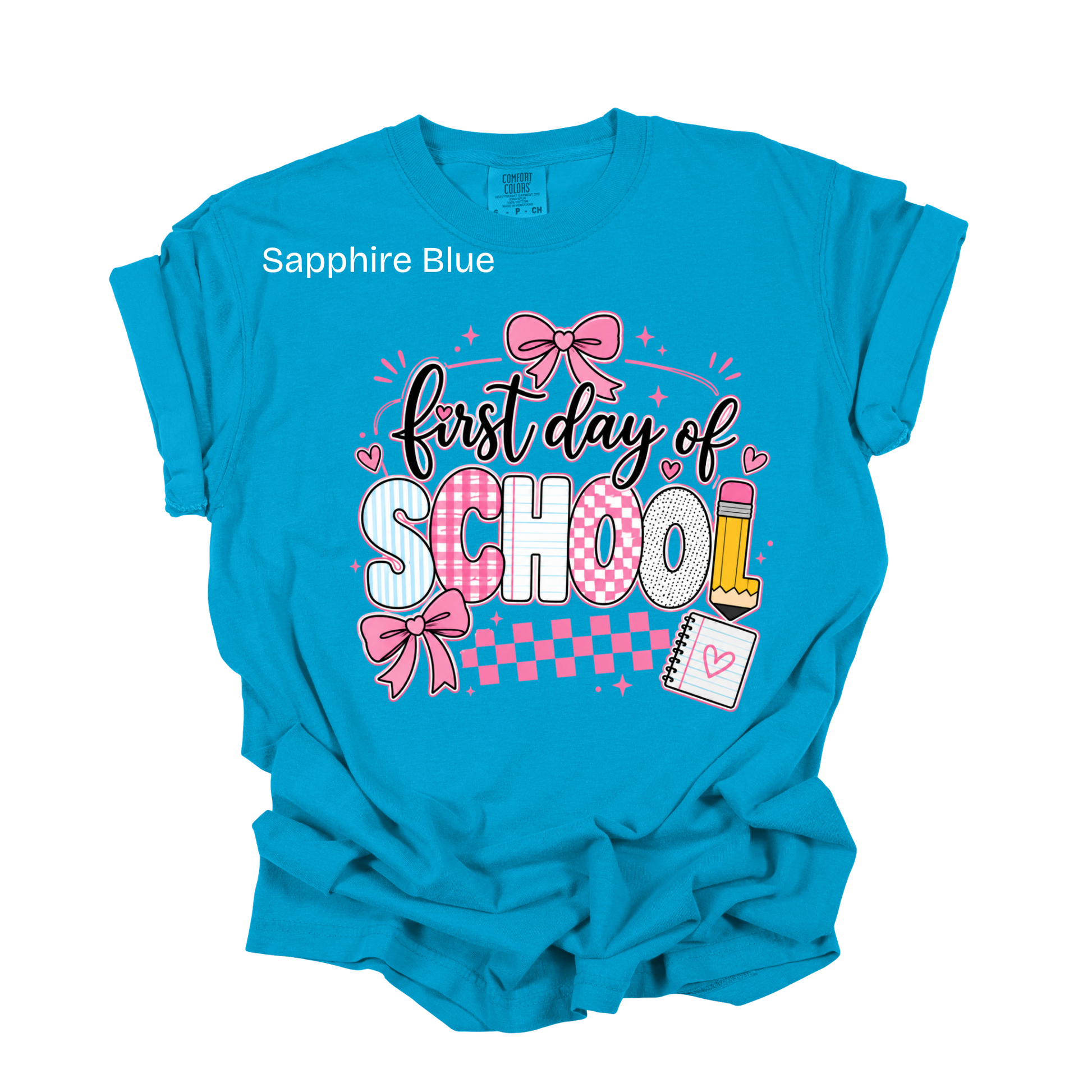 A bright turquoise blue short-sleeve t-shirt with a 'first day of SCHOOL' graphic on the front. The graphic features pink bows, checkered patterns, and school-themed illustrations like a pencil and notebook.